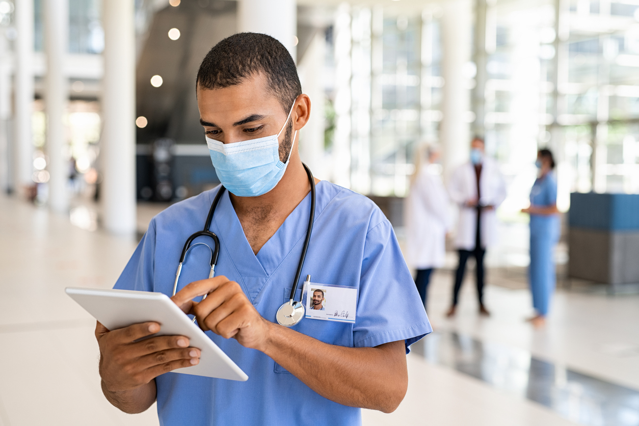 Male nurse consults ipad in corridor of hospital